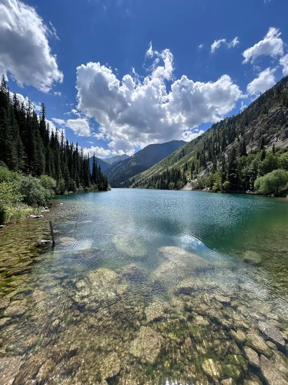 Clear turquoise lake with forest and cloudy mountain backdrop