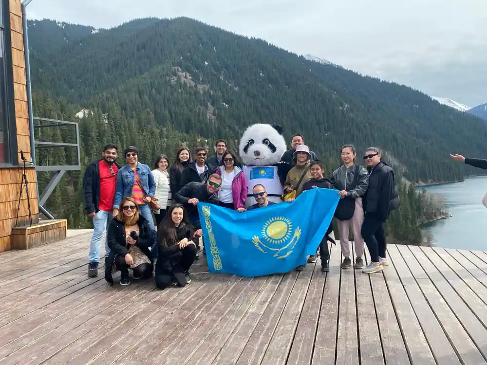 Large group holding Kazakhstan flag with panda mascot outdoors