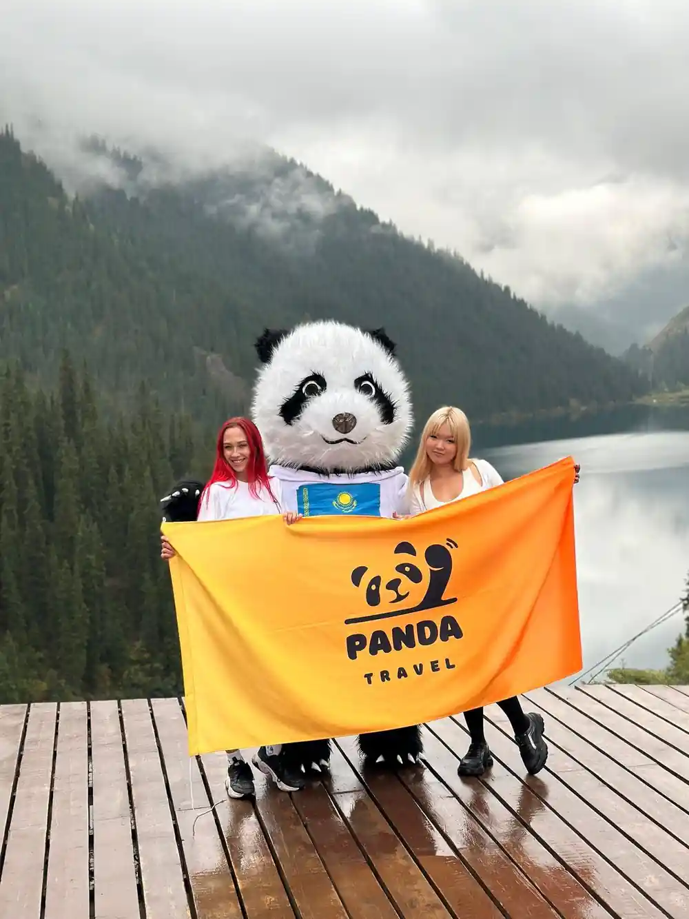 Two young women with panda mascot by mountain lake