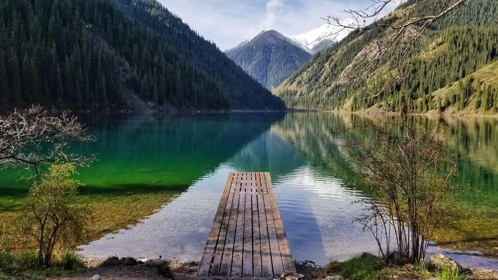 Wooden dock extending into turquoise lake surrounded by forested mountains