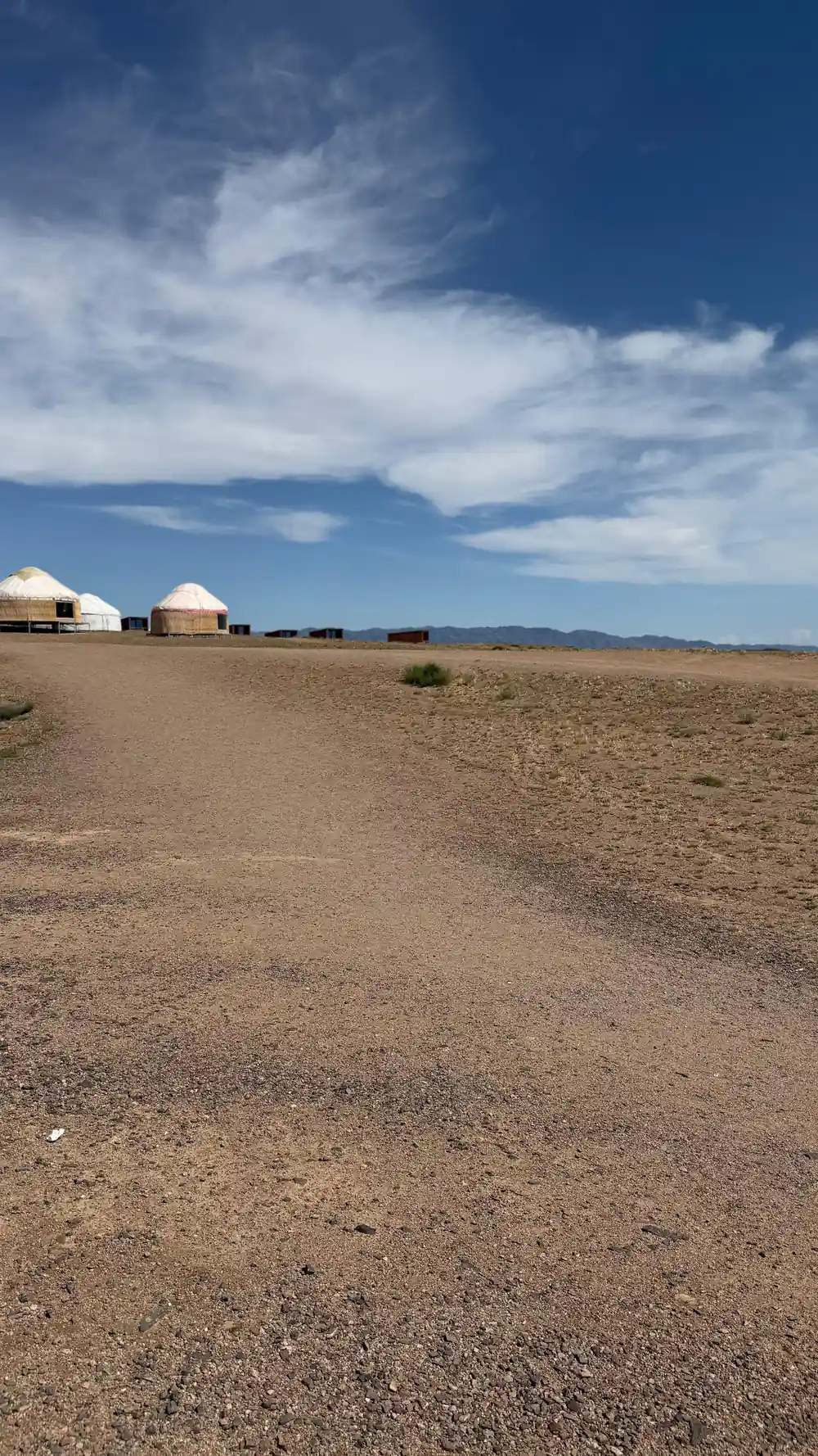 Yurt dwellings on flat arid plain with mountains background